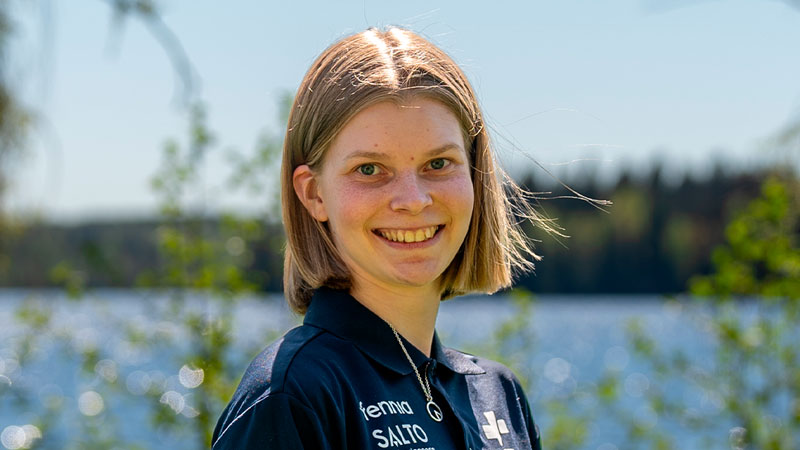 Venla Salo hymyilemässä kameralle aurinkoisessa säässä vesistöä ja vihreää kasvustoa vasten.